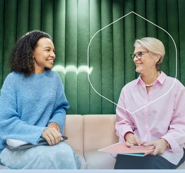 Two therapists speaking in a comfortable office with a blue geometric frame overlay.