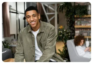 A smiling person seated in a workplace lounge.