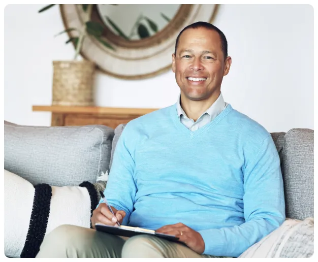 A therapist smiling while seated on a couch in a calm office.